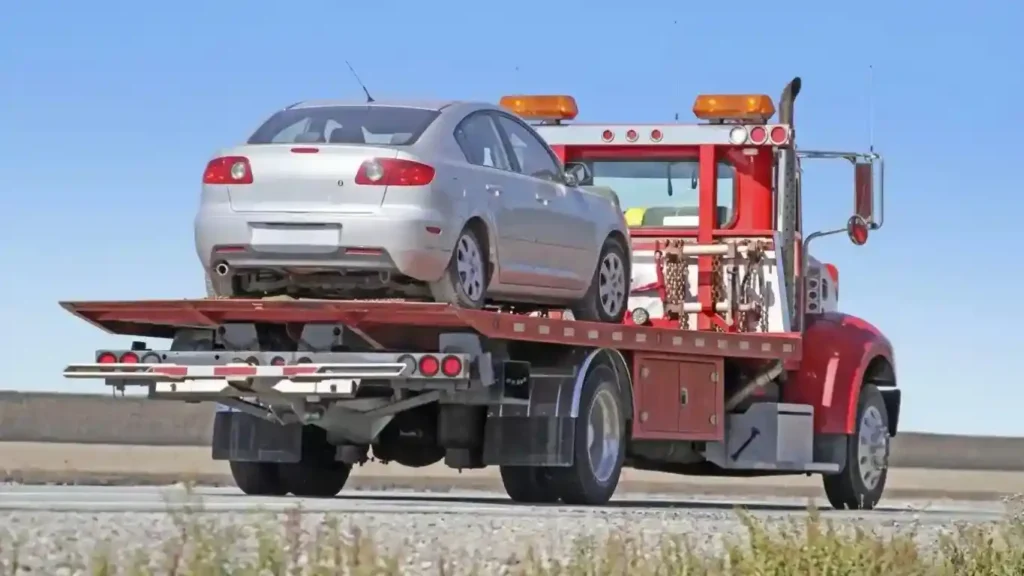 A red flatbed tow truck of 'Tow Truck Calgary' carries a silver car on an asphalt road in Calgary, Alberta.