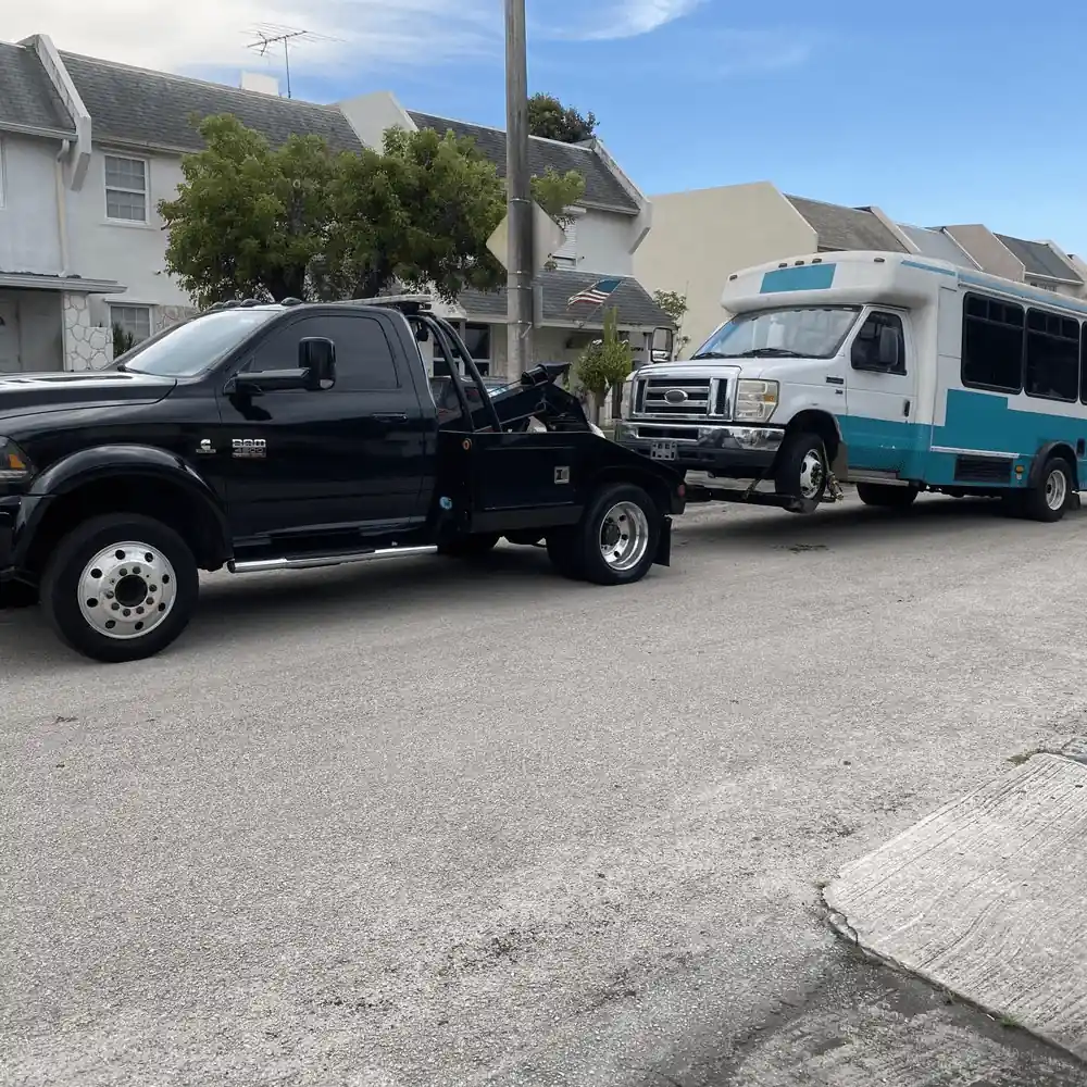 Black tow truck towing broken down shuttle bus on residential street in Airdrie Calgary.