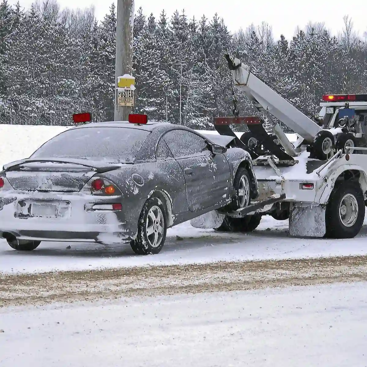 Tow truck recovering snow covered damaged car in winter conditions across Calgary service areas.