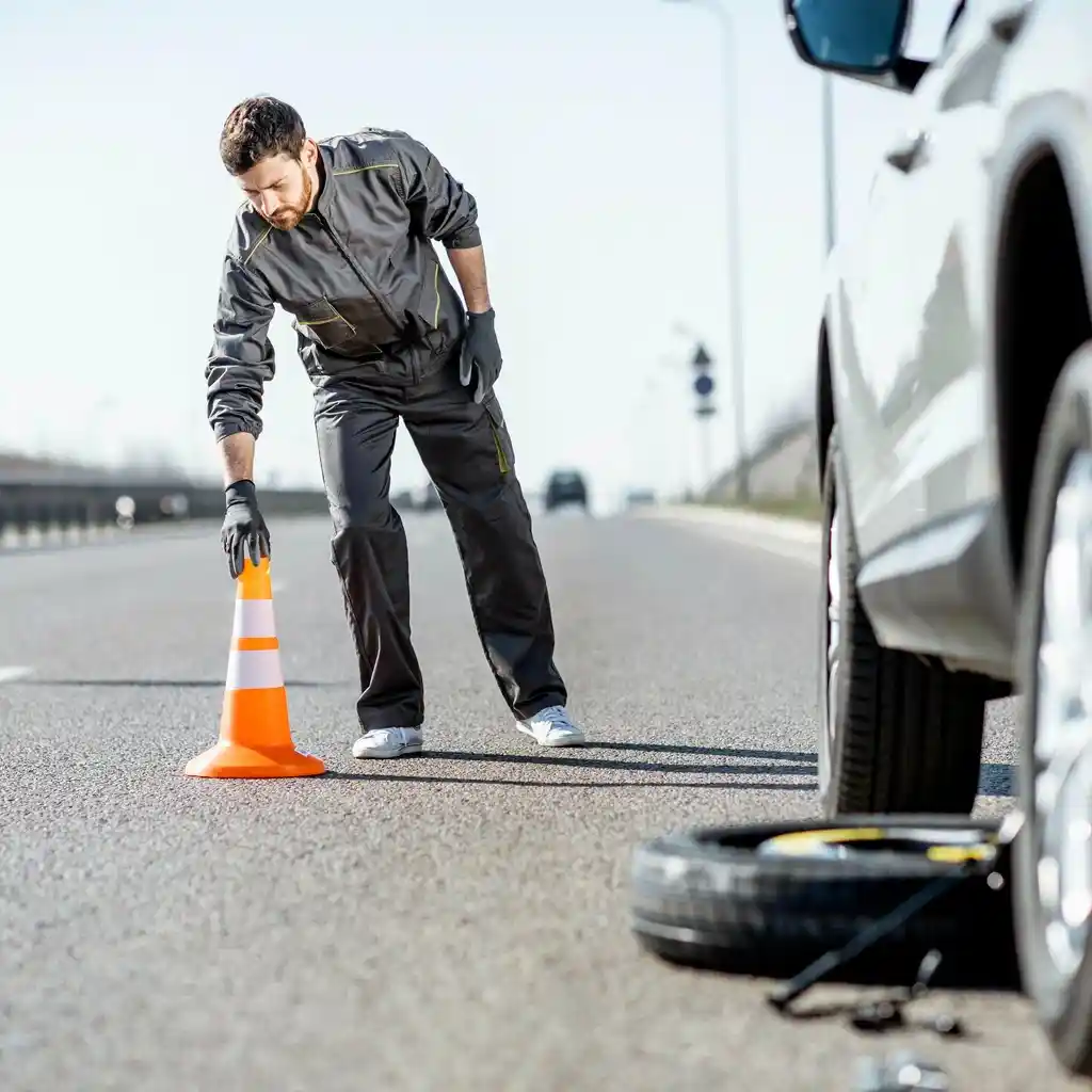 Roadside technician placing traffic cone near flat tire on highway – Tow Truck Calgary.