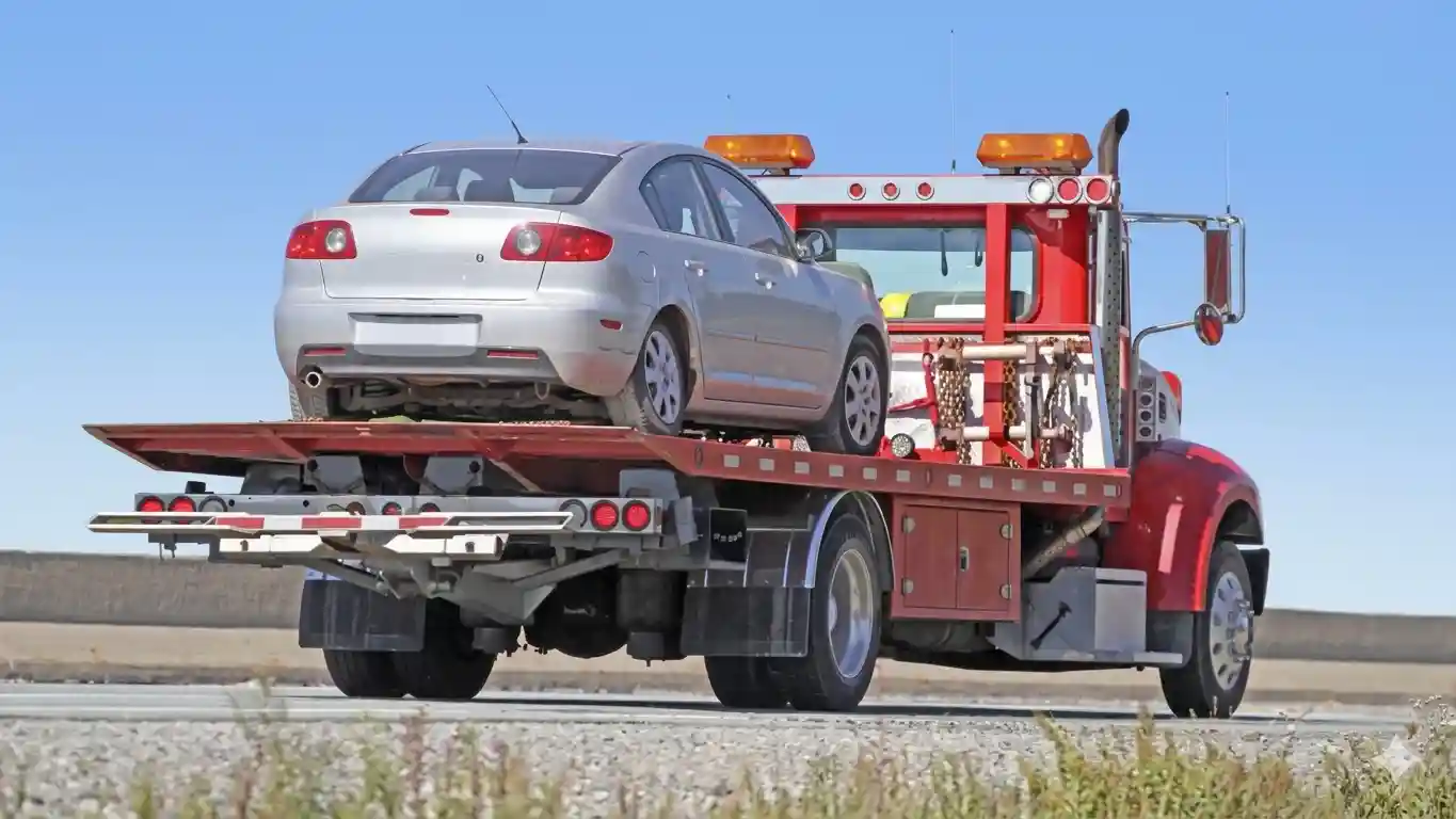 A red flatbed tow truck of 'Tow Truck Calgary' carries a silver car on an asphalt road in Calgary, Alberta.