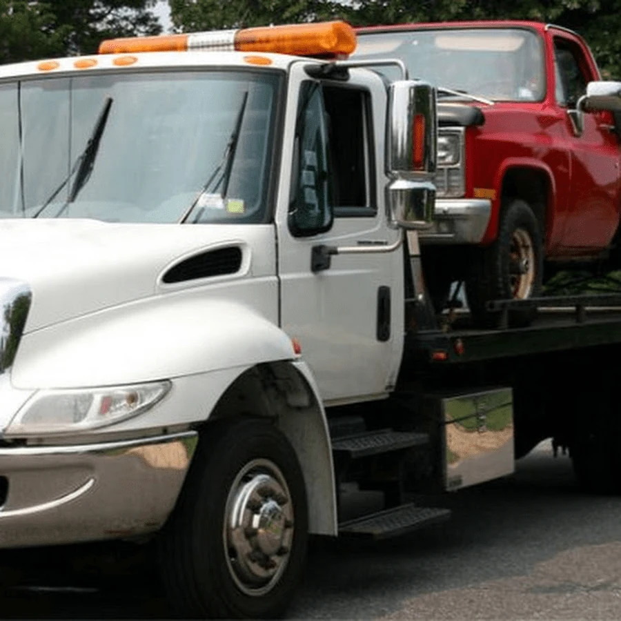 White flatbed tow truck transporting red pickup truck across Calgary service areas